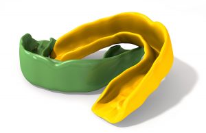 Two regular yellow and green moulded sports gum guards on an isolated background